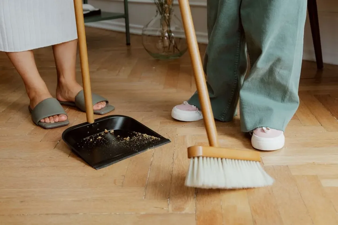 Personnes nettoyant un parquet en bois avec un balai et une pelle.